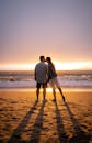 一对夫妇在日落时分在沙滩上分享一个浪漫的吻，阴影向大海延伸