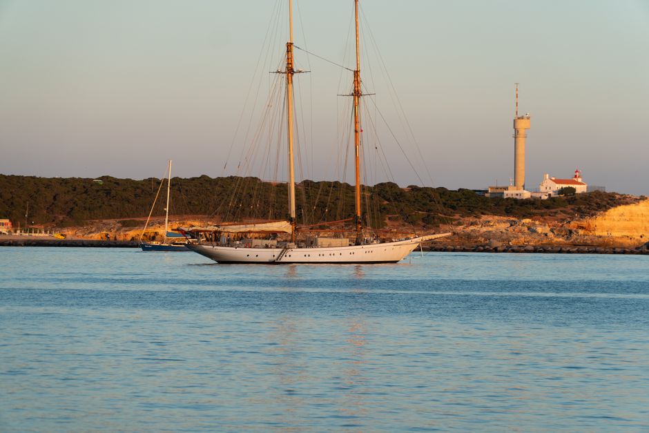 Elegant sailboat near Ponta do Altar Lighthouse at sunset in Portugal's scenic harbor.