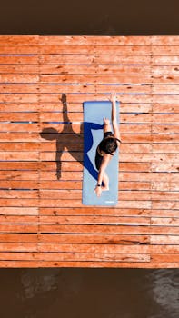 Woman doing yoga on a deck over water, captured from above.