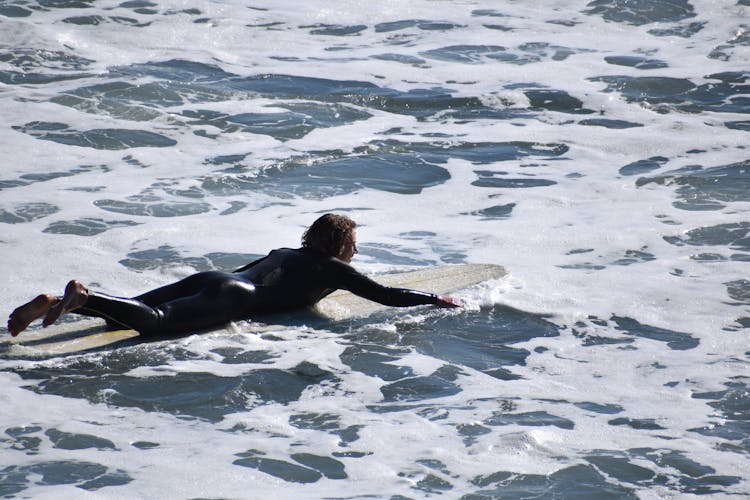 Male Surfer Paddling On Surfboard In Water