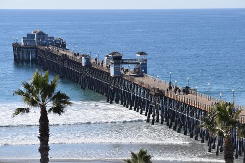 Free A beautiful long pier extending into the ocean, surrounded by palm trees and gentle waves. Stock Photo