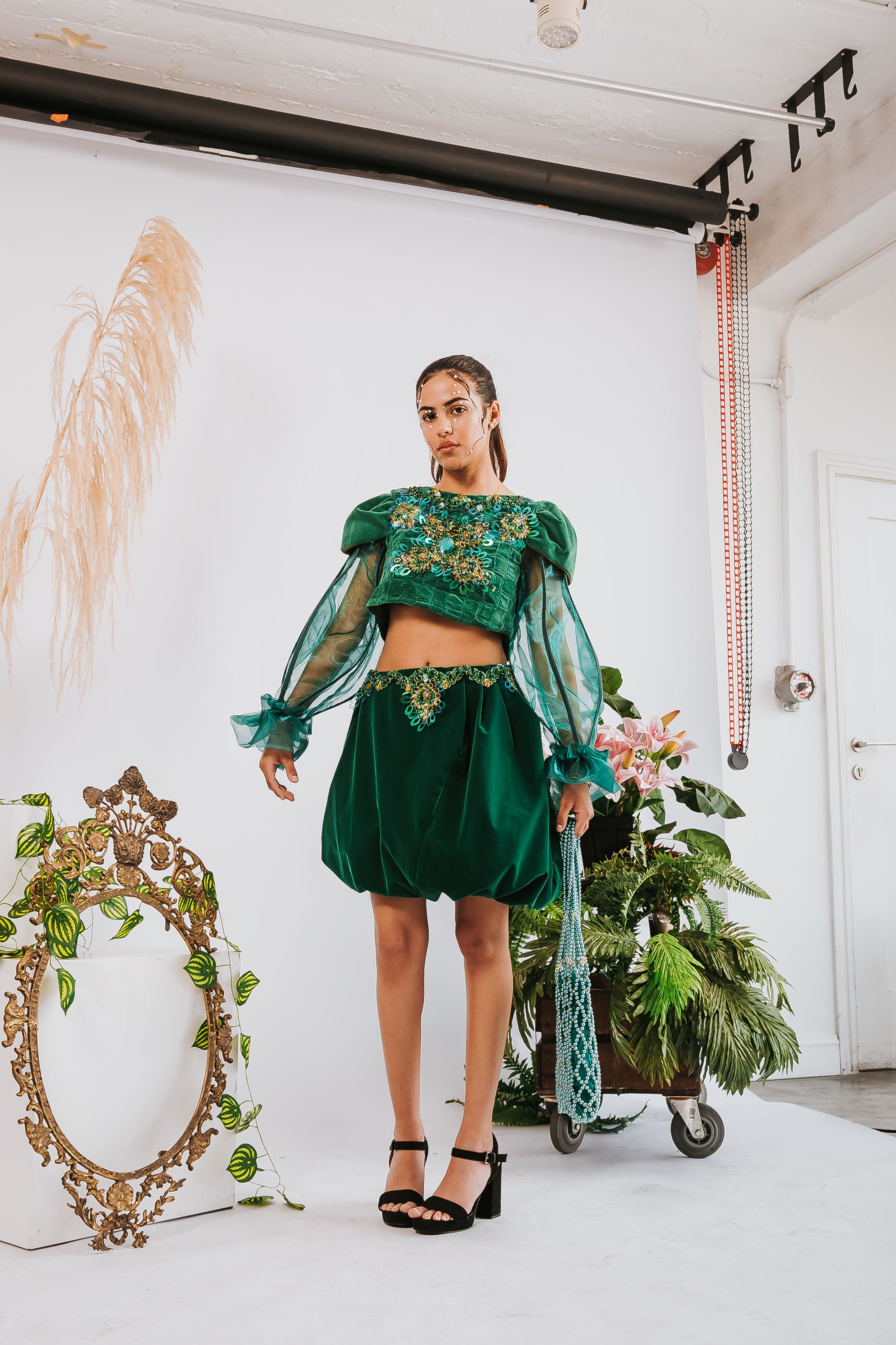 Mulher elegante posando em um conjunto verde estiloso com decoração floral em um ambiente de estúdio.