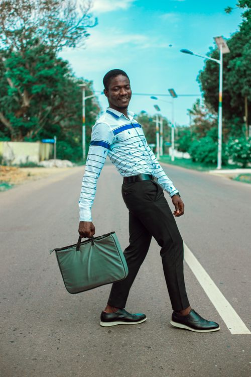 Free Smiling African man stylishly posing with a bag on a peaceful street in Accra, Ghana. Stock Photo