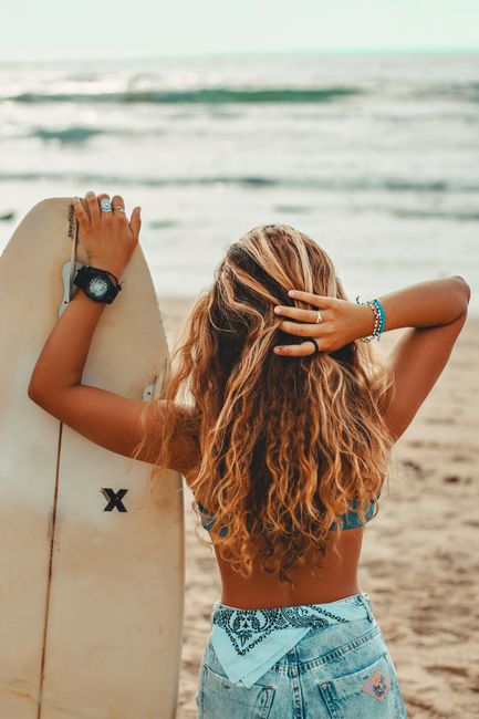 Blonde woman with surfboard standing on sunny beach, enjoying summer vibe.