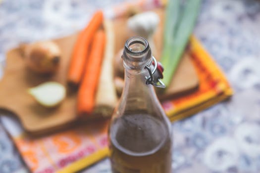 Close-up of a glass bottle with vegetables on a wooden cutting board, capturing a rustic kitchen vibe.