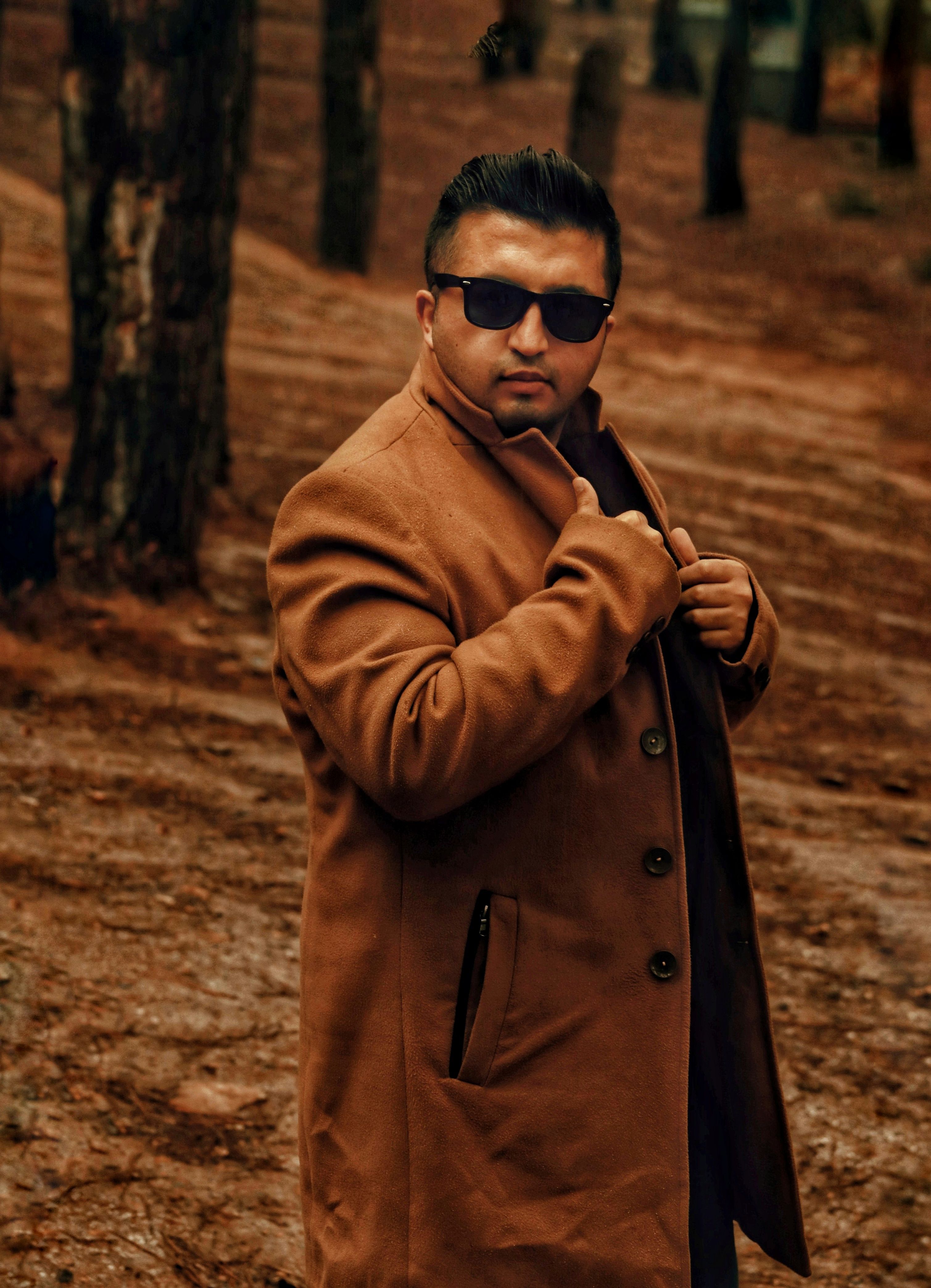 Stylish man in sunglasses and coat posing in autumn forest setting.