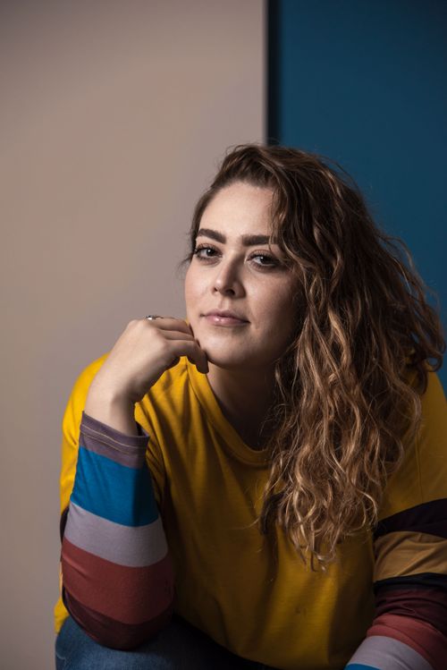 Free A thoughtful portrait of a woman wearing a vibrant yellow sweater, showcasing her curly hair and confident expression. Stock Photo