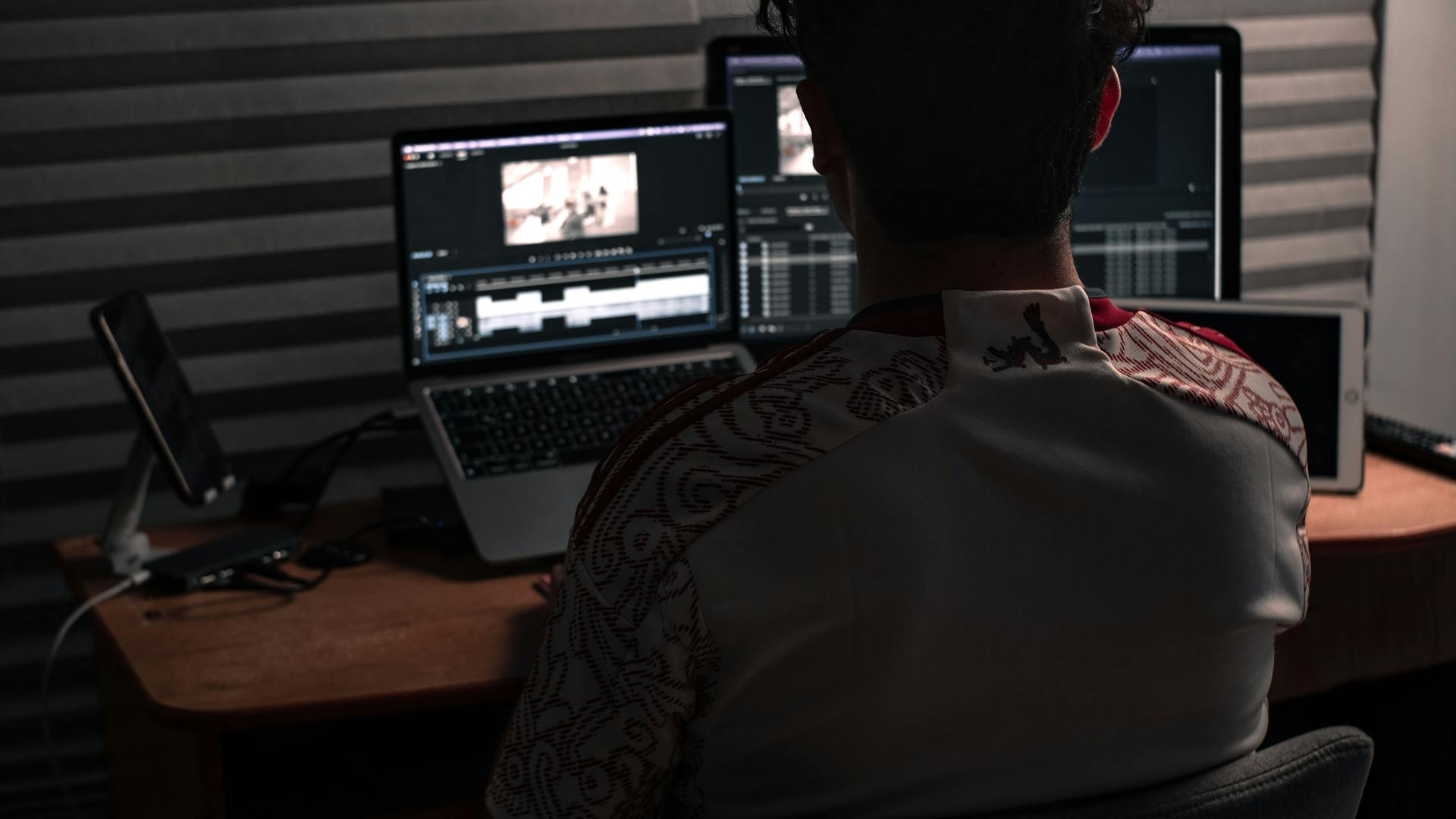 Man sitting at desk working on video editing software with dual monitors in an office.