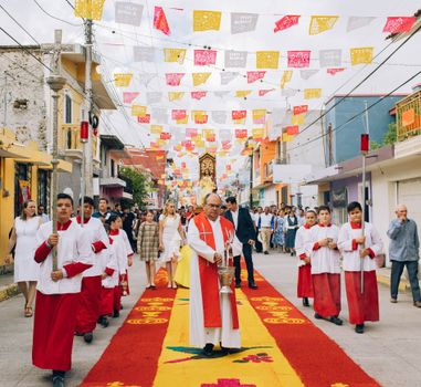 Vibrant religious procession with participants in traditional attire on decorated street in Mexico.