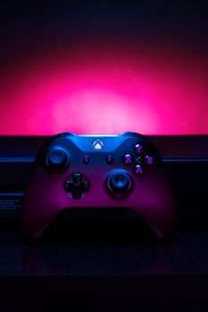 Close-up photo of an Xbox controller illuminated by vibrant purple and pink neon lights.