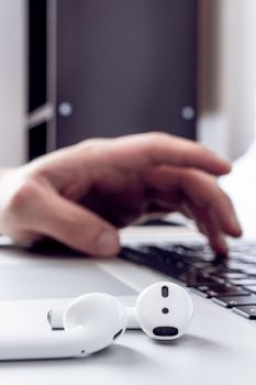 Close-up shot of wireless AirPods on laptop with hand typing in background, ideal for tech themes.