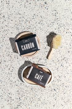 Flat lay of artisanal soap bars labeled 'Carbón' and 'Café' with a natural brush on a speckled surface. - Fotografer Sidoarjo