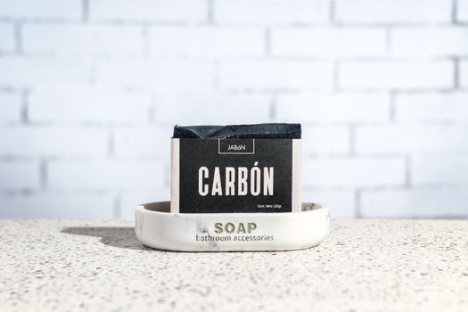 Close-up of handcrafted charcoal soap on a marble tray against a white brick wall. - Fotografer Sidoarjo