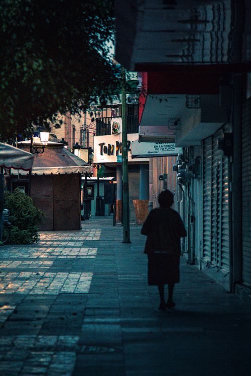 Free A lone silhouette walking along a quiet urban street in the evening light. Stock Photo