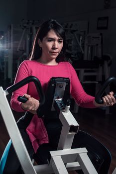 Woman focused on strength training with machine in gym, promoting a healthy lifestyle.