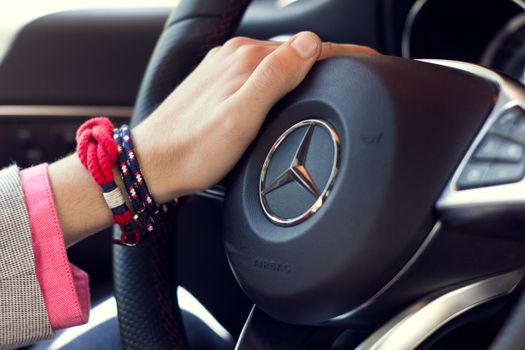 A hand adorned with bracelets on a Mercedes-Benz steering wheel in a car interior.