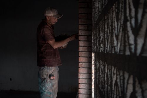 Free A construction worker laying bricks inside a dimly lit room, illustrating dedication. Stock Photo
