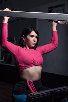 Young woman exercising in gym, wearing a pink long-sleeve top, focused on a healthy lifestyle.