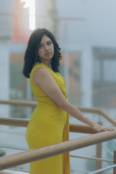 Stylish woman in a yellow dress posing on a balcony indoors. Perfect for fashion themes.