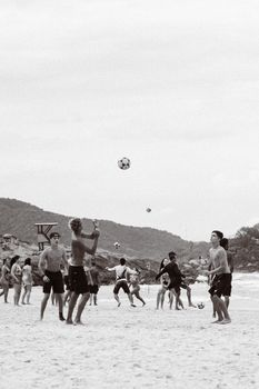 A lively group of young adults playing soccer on a sandy beach, enjoying a sunny day.