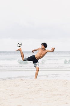A shirtless man showing off soccer skills on a scenic beach.
