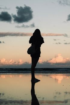 Silhouette of a woman on a reflective beach at sunset, capturing a peaceful moment.