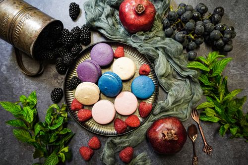 Free Colorful arrangement of macarons with fruits like pomegranates, grapes, and berries. Top view. Stock Photo