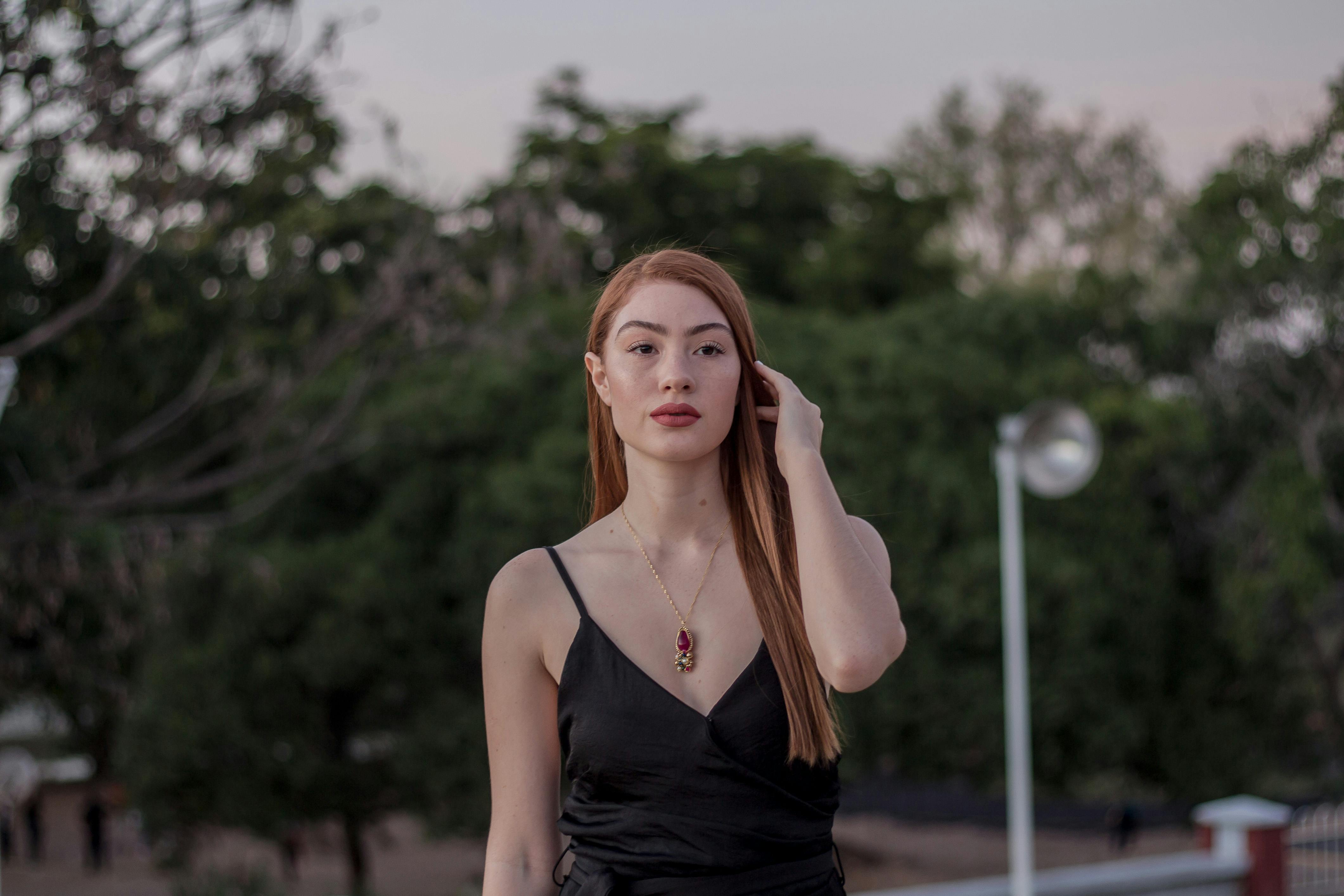 黄昏时分，一位身着黑色连衣裙、佩戴红色项链的时尚女士在户外摆姿，尽显优雅与自信