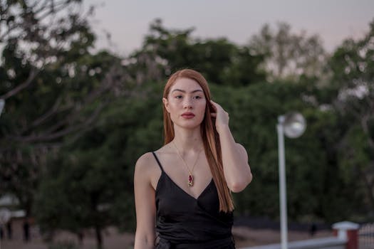 黄昏时分，一位身着黑色连衣裙、佩戴红色项链的时尚女士在户外摆姿，尽显优雅与自信