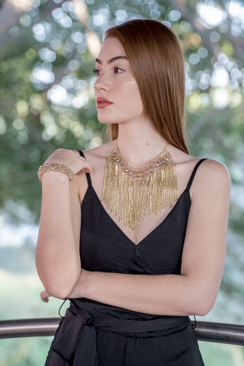 Free A stylish woman in a black dress showcasing a luxurious gold necklace outdoors. Stock Photo