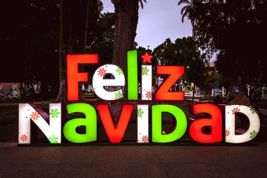 Festive 'Feliz Navidad' sign glowing at night in a Mérida park, perfect for Christmas themes.
