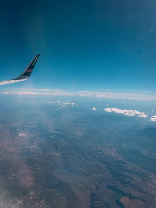 Free View from airplane wing showcasing clouds and landscape below under a clear blue sky. Stock Photo