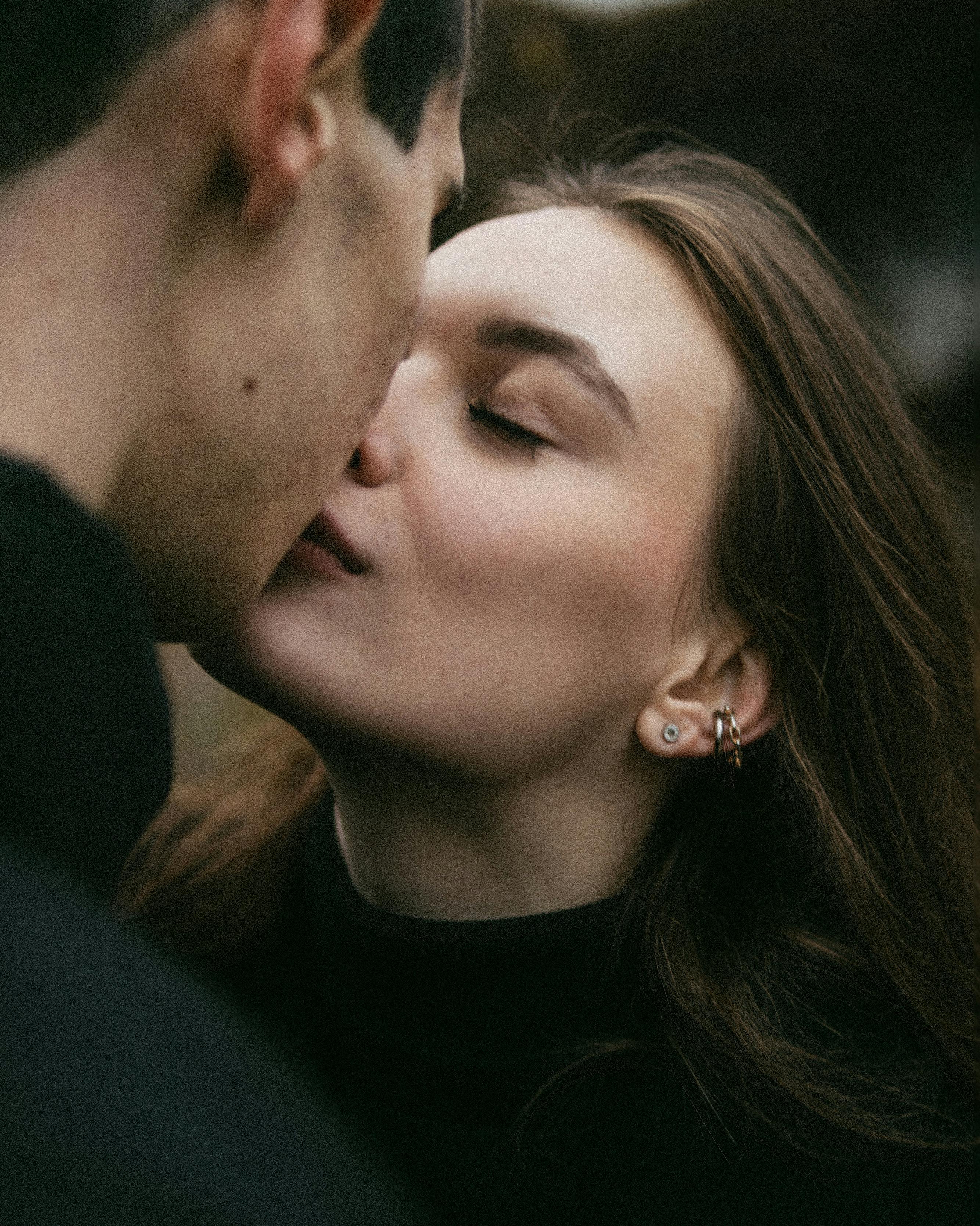 An intimate close-up shot of a couple sharing a romantic kiss outdoors.