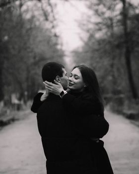 A black and white photo of a couple embracing in a forested path, showcasing love and connection.