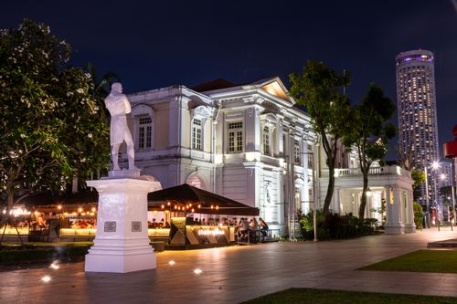 Free An illuminated historic building with a statue and city lights at night in Singapore, capturing urban charm. Stock Photo