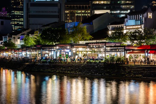 A lively night scene of restaurants and reflections along the Singapore River.