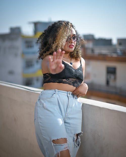 Woman in Brassiere and Ripped Jeans Leaning on Concrete Fence