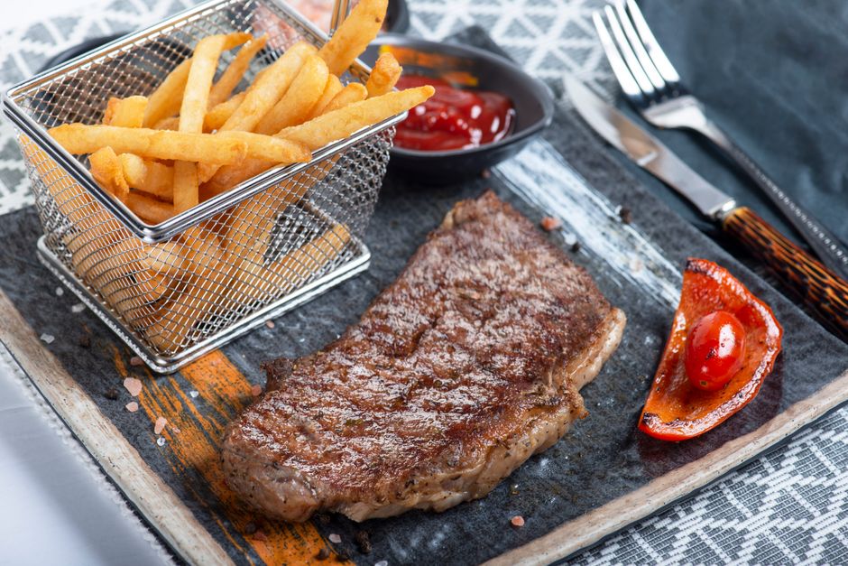 A pile of thick-cut, skin-on steak fries with crispy golden-brown edges and a fluffy interior, served alongside a burger and a ramekin of ketchup.