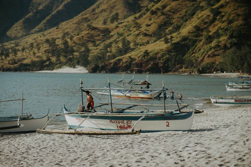 Free Traditional boats rest on a sandy beach with lush, green hills in the background. A tranquil seaside scene. Stock Photo