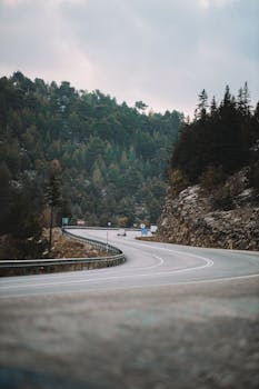 A winding road through mountainous terrain with dense forest, ideal for travel and adventure themes.