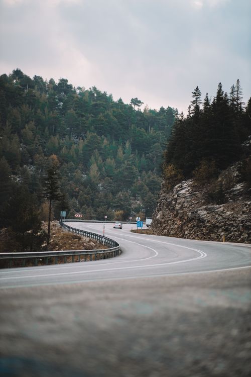 Free A winding road through mountainous terrain with dense forest, ideal for travel and adventure themes. Stock Photo