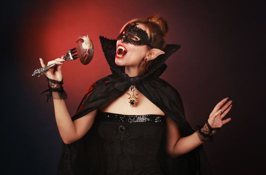 Mysterious woman dressed as a vampire with a gothic mask and cape, holding a fork