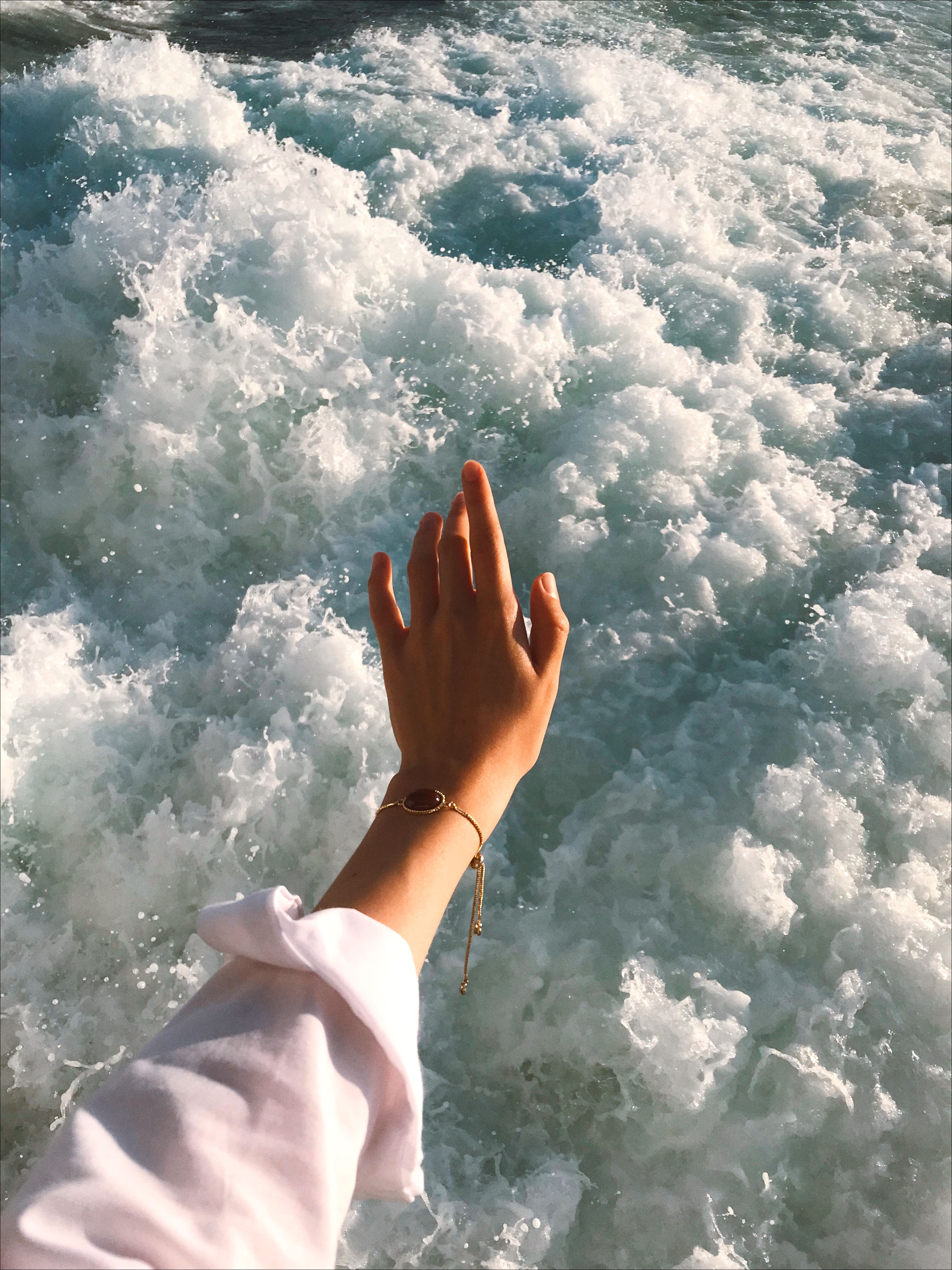A hand with bracelet extends towards the crashing ocean waves, showcasing vibrant motion and elegance.