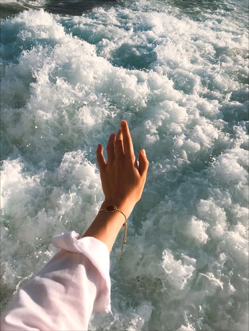 A hand with bracelet extends towards the crashing ocean waves, showcasing vibrant motion and elegance.