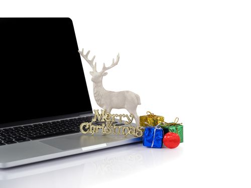 Free A laptop with Christmas decorations including a reindeer and colorful gifts on a white surface. Stock Photo