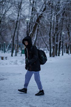 A young boy dressed in winter clothing walking through a snow-covered park, capturing the essence of a cold winter day.