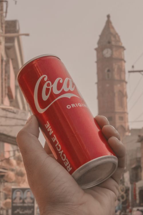 Free A hand holding a Coca-Cola can in front of a historic tower in an urban setting. Stock Photo