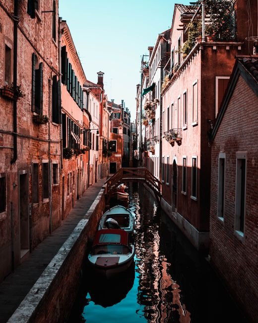Scenic view of a narrow canal in Venice with traditional architecture and moored boats reflecting the warm tones of sunset.