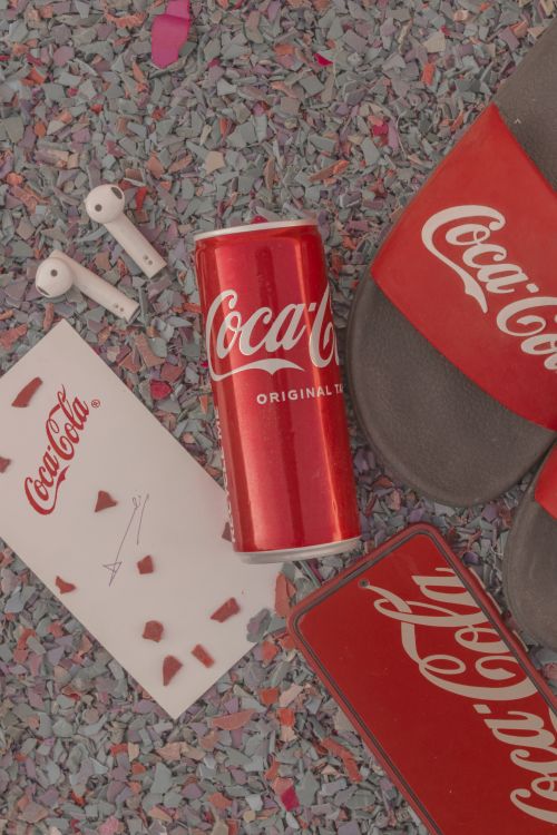 Free Coca-Cola can with accessories, featuring branded sandals and headphones on a colorful backdrop. Stock Photo