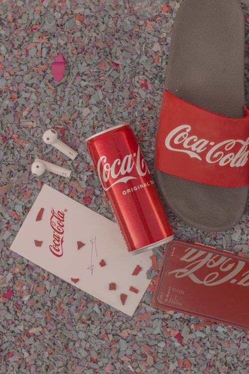 Free Flat lay featuring Coca-Cola can, sandals, and accessories on textured ground. Stock Photo
